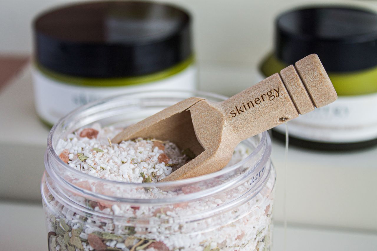 Close-up of a jar filled with bath salts and a wooden scoop labeled 'skinergey'.