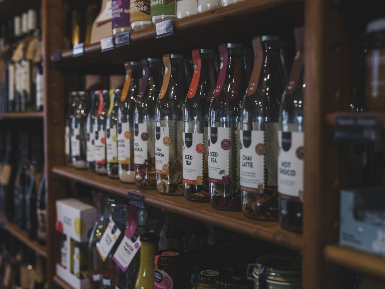 A variety of bottled beverages arranged on wooden shelves in a cozy shop setting.