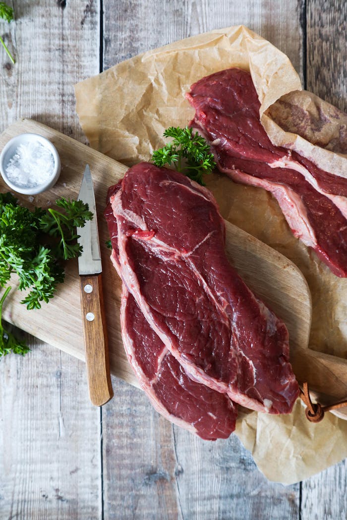 Raw steak on wooden board with knife and parsley, perfect for culinary themes.